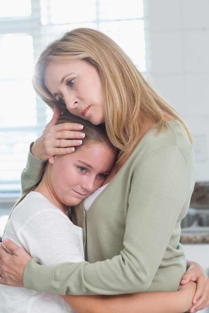 Sad little girl hugging her mother at home in the kitchen
