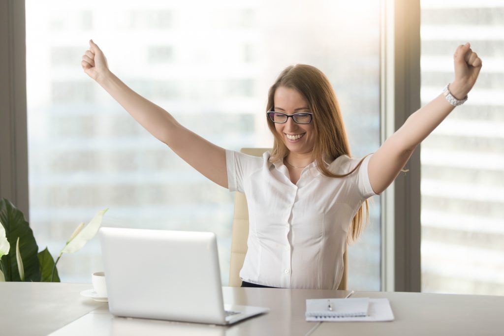 Excited smiling businesswoman celebrating business success at workplace, raising hands looking at laptop screen, feeling happy about great win, good news online, positive result, passed exam, got job