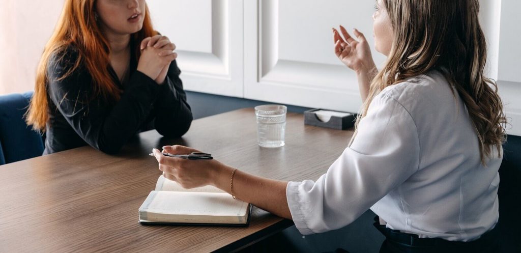 Image of a woman talking while sitting at a table with another woman. If you struggle with anxiety discover how neurofeedback therapy in Englewood, CO can help!