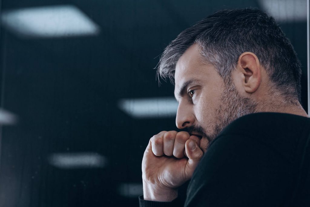 Image of an anxious man holding his fist to his mouth and wearing a black shirt. If you struggle with anxiety, learn how effective neurofeedback therapy for anxiety in Englewood, CO can help you cope.