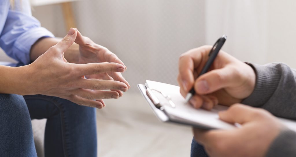 Image of someone in therapy speaking with a therapist who writes on a clipboard. Overcome your anxiety symptoms in healthy way with the help of neurofeedback therapy for anxiety in Englewood, CO.