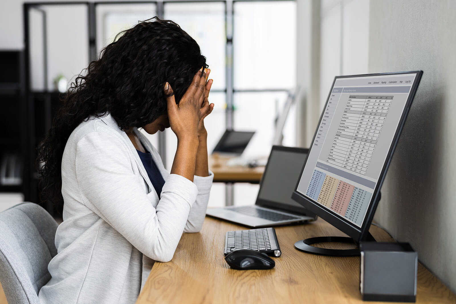 Image of a professional woman sitting at a desk at work covering her face with her hands feeling stressed. Do you struggle to manage your anxiety? Learn how neurofeedback therapy for anxiety in Englewood, CO can help you manage your symptoms.