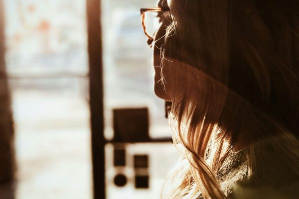 Image of a woman wearing glasses staring out a window as the sun shines on her face. Discover how EMDR therapy in Englewood, CO works and how it can help you manage your trauma, anxiety, and more.
