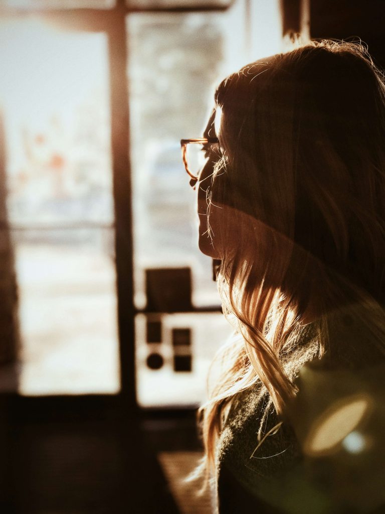 Image of a woman wearing glasses staring out a window as the sun shines on her face. Discover how EMDR therapy in Englewood, CO works and how it can help you manage your trauma, anxiety, and more.