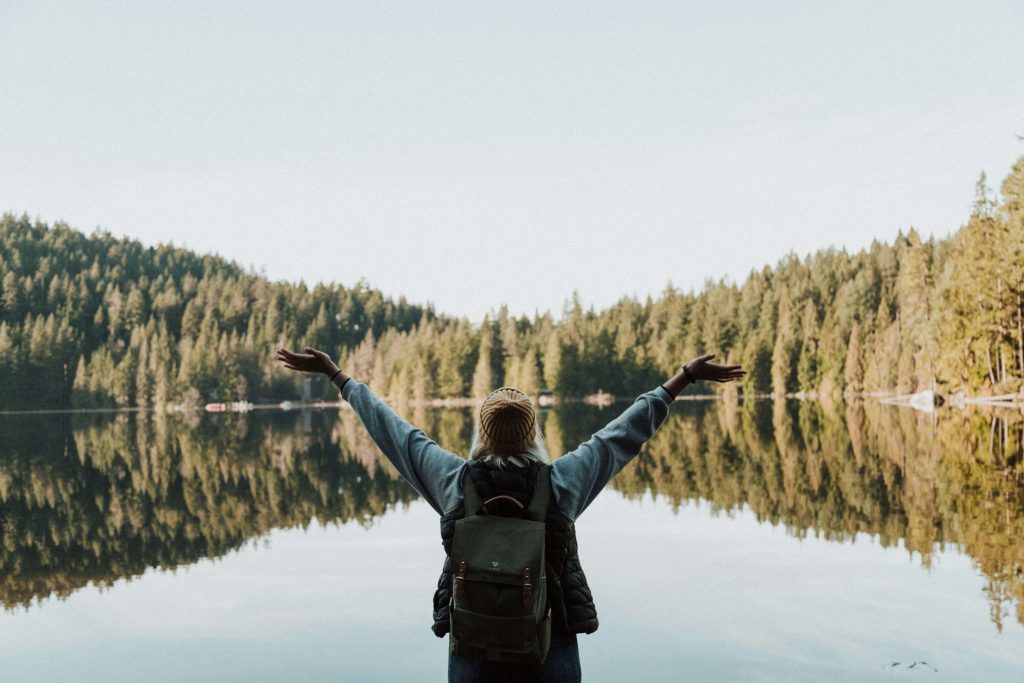 Image of a woman wearing a backpack standing in front of a lake with her arms in the air. If you struggle with anxiety, depression, trauma, and more, learn how EMDR therapy in Littleton, CO can help you.