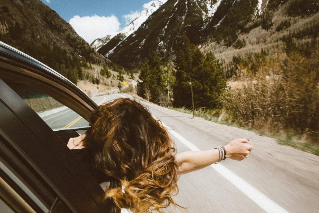 Image of a woman hanging out of a car window driving down a highway through the mountains. Learn to effectively cope with your ADHD symptoms with the help of neurofeedback therapy in Denver, CO.