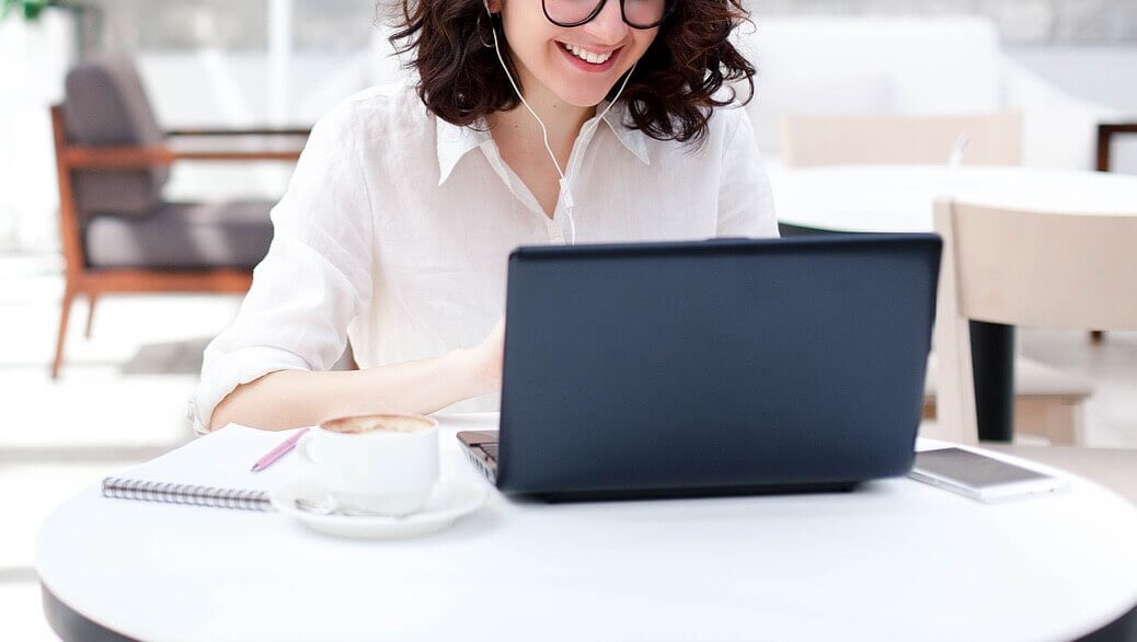 Image of a smiling woman sitting at a table working on a laptop. If you struggle with your past trauma, learn how EMDR therapy in Denver, CO can help you cope and begin healing.