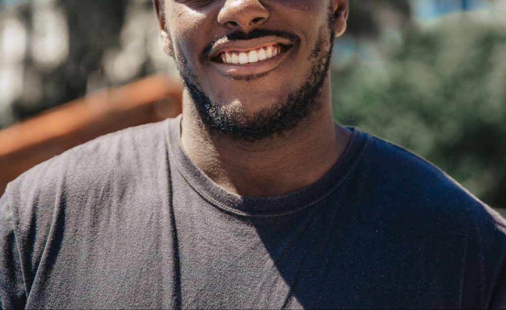 Image of a smiling man wearing a black shirt standing outside on a sunny day. Learn to manage your TBI with the help of neurofeedback therapy in Denver, CO.