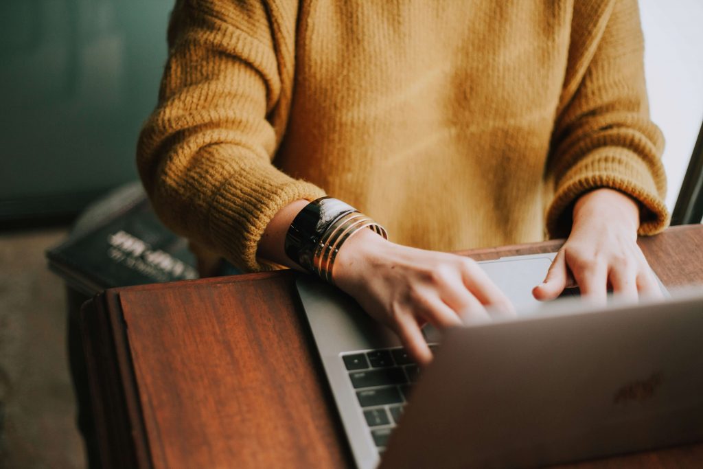 Image of a woman wearing a mustard sweater typing on a laptop. Find easy ways to access therapy with the help of telehealth therapy in Denver, CO.