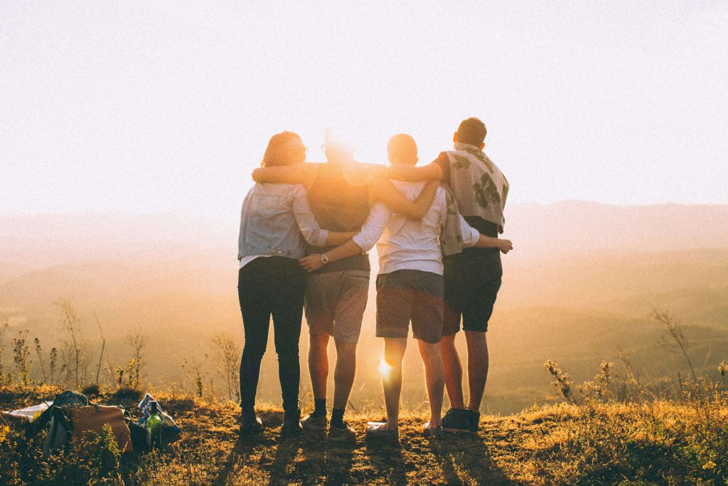 Image of a group of teens with their arms on each others shoulders looking down from the top of a hill while the sun sets. Discover how teen counseling can help support your team and a convenient way with telehealth therapy in Denver, CO.