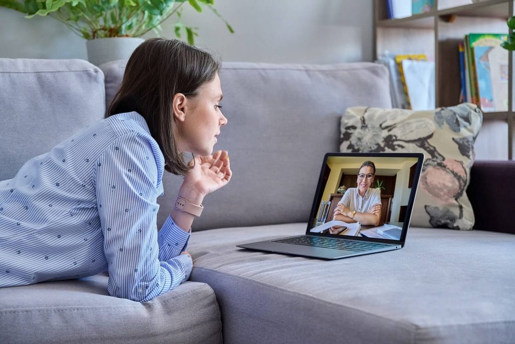 Image of a woman laying on a couch, speaking to a online therapist on a laptop. Begin overcoming your anxiety, depression, and more with the help of telehealth in Denver, CO.