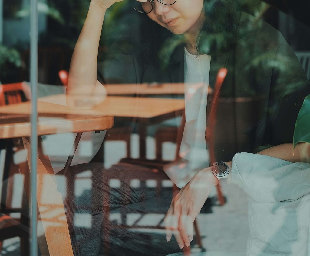 Image of an upset woman behind a window sitting at a table in a cafe. Learn how EMDR therapy in Denver, CO can help you cope and work to improve your trauma symptoms.