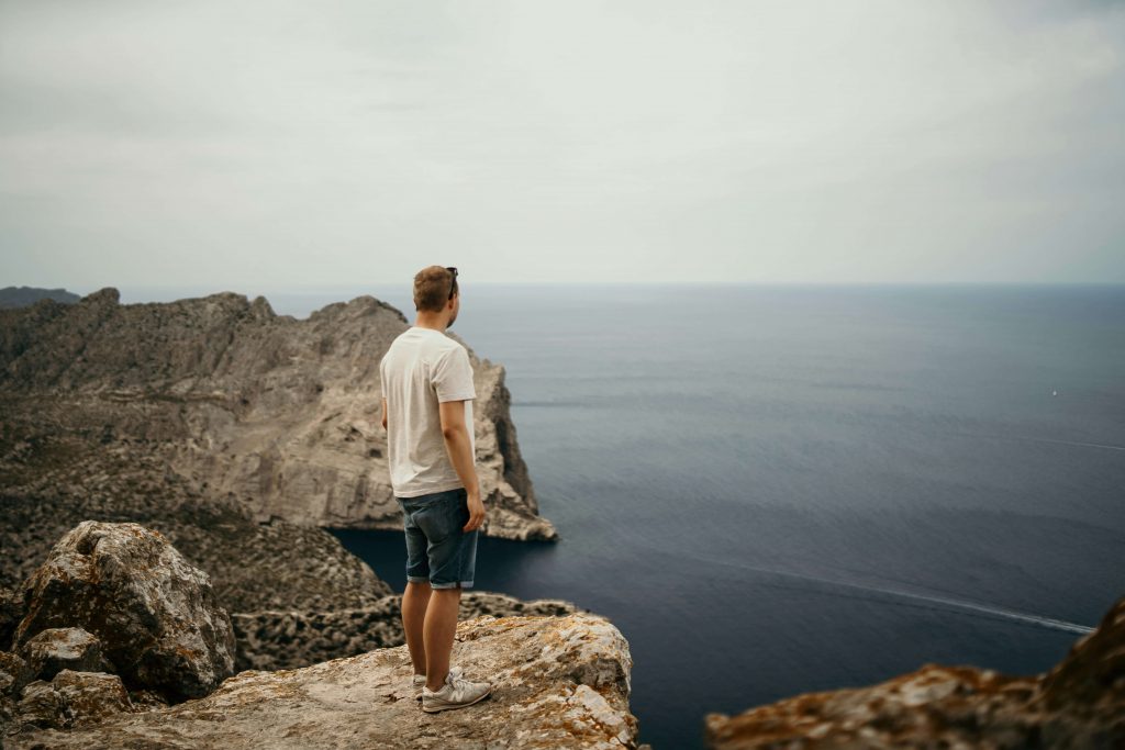 Image of a man standing on top of a rocky cliff overlooking the ocean on a cloudy day. Begin healing and managing your past trauma symptoms with the help of EMDR therapy in Denver, CO.