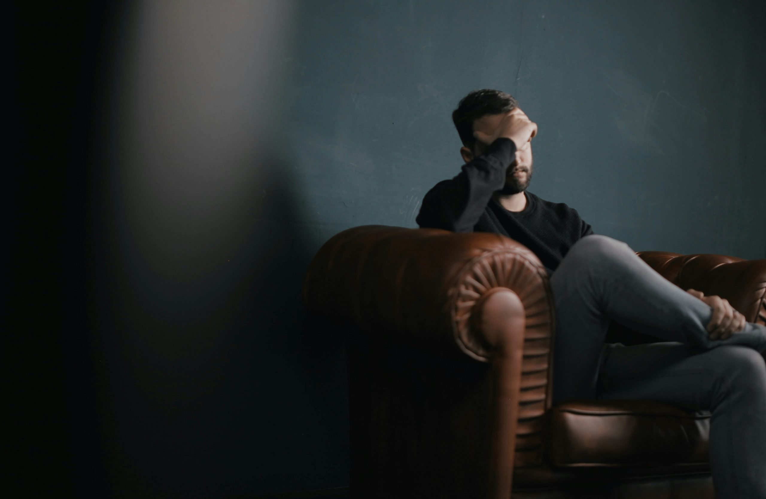 Image of a stressed man with his hand on his forehead sitting on a leather couch. Discover how you can effectively manage your stress and anxiety with the help of an anxiety therapist. Find support with anxiety therapy in Littleton, CO.