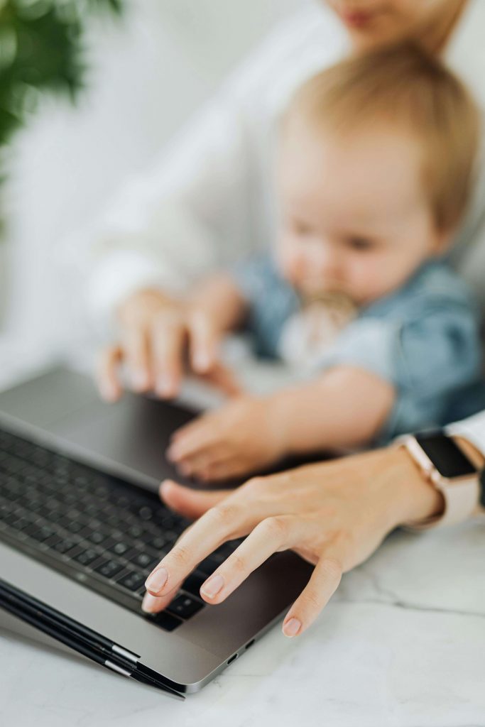 mother typing with baby | online therapy in colorado | online therapy that takes insurance | online treatment for depression in colorado | Greenwood Village, CO | Littleton, CO | Englewood, CO A mother types on a laptop with her baby on her lap, showing the flexibility of online therapy in Colorado, including therapy for moms and online therapy that takes insurance.