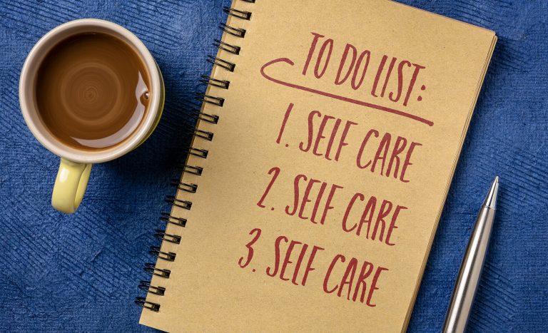 A coffee cup beside a notebook with “Self Care” written multiple times, reflecting how a maternal mental health therapist encourages therapy for moms, support for maternal anxiety, and guidance from a postpartum therapist near me.