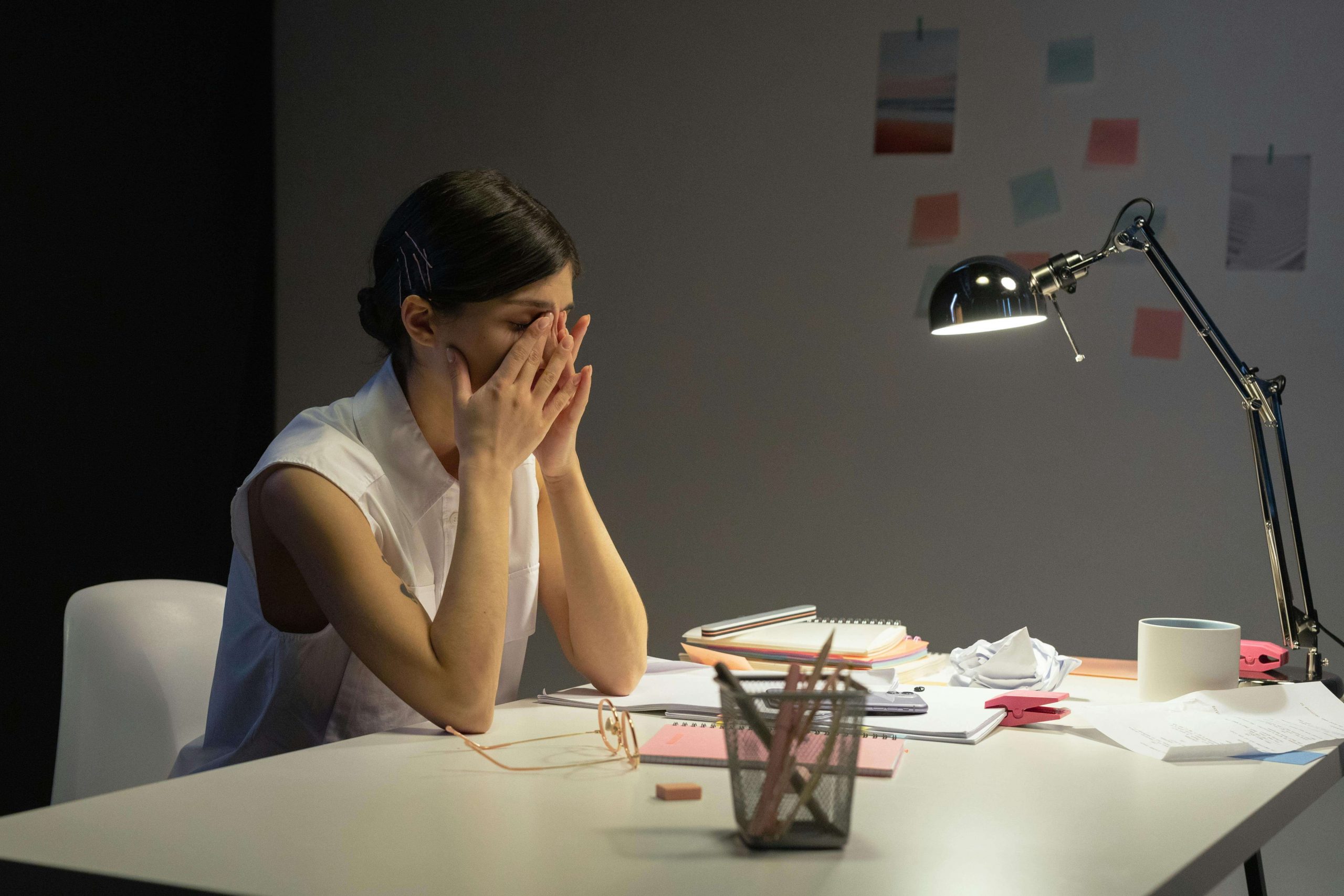 An overwhelmed woman sits at her desk with her head in her hands, highlighting the importance of ADHD testing in Littleton, CO, ADHD test for women, and searching for ADHD evaluation near me for support. 