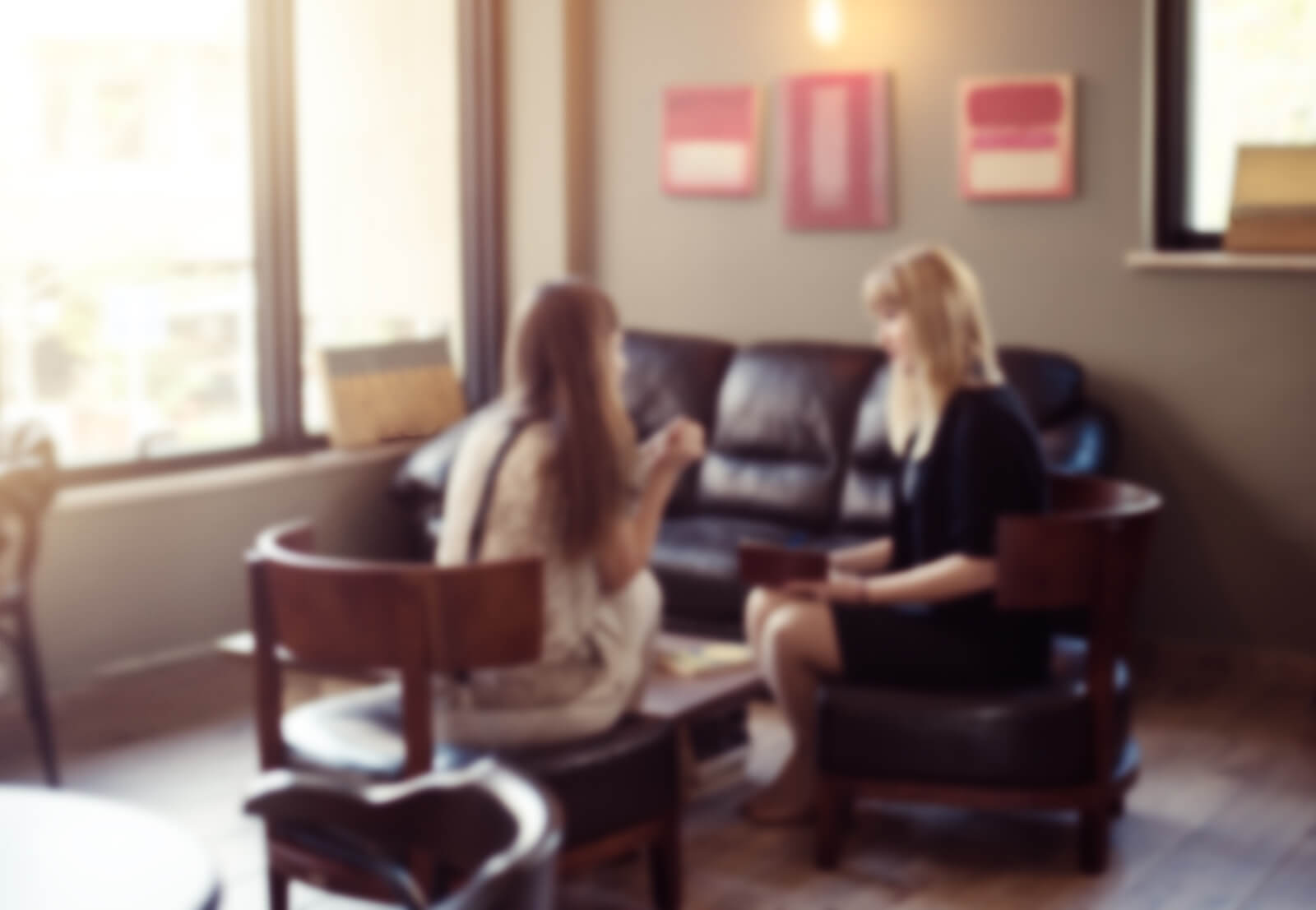 Two women sit in a cozy, softly lit therapy office, engaged in conversation. This welcoming space reflects the environment clients experience when receiving co-parenting counseling, neurofeedback Denver services, or online therapy in Denver, CO. Compassionate care from a therapist in Hampden, CO is just a conversation away.
