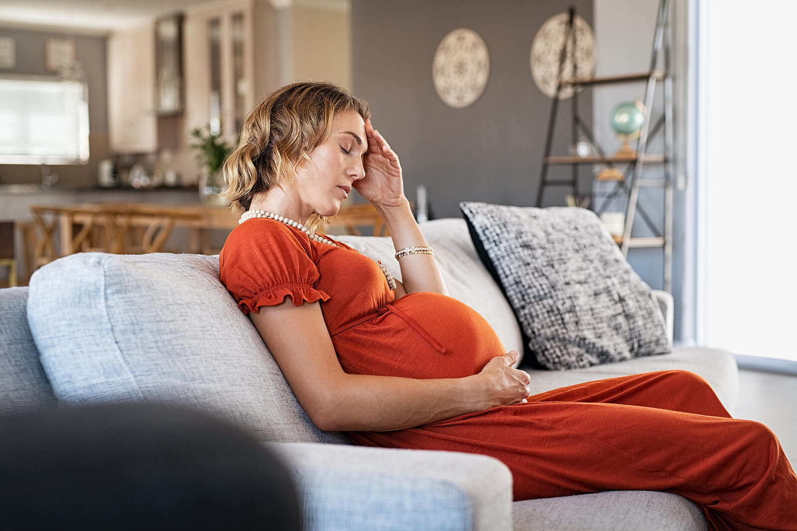 stressed pregnant woman | maternal mental health therapist | postpartum anxiety therapy in greenwood village, co | greenwood village, co | englewood, co | denver, co Tired pregnant person resting on a couch with a hand on their head, illustrating how therapy for moms and support from a maternal mental health therapist or postpartum therapist can ease overwhelm through postpartum anxiety therapy in greenwood village, co.