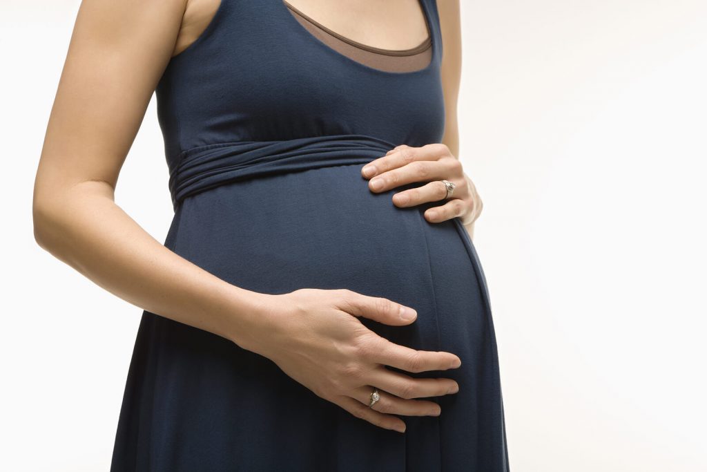 Pregnant person in a blue dress gently holding their belly, symbolizing the need for therapy for moms with a compassionate maternal mental health therapist, postpartum therapist, or postpartum depression therapist near me during pregnancy and after birth.